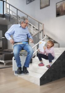 Senior and child smiling at bottom of curved stairlift in South Wales home